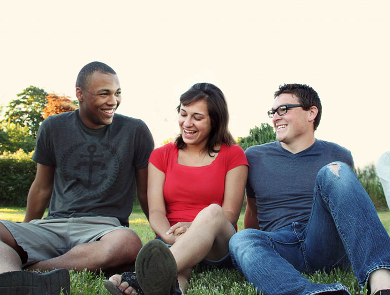 Smiling women and men sitting on green grass